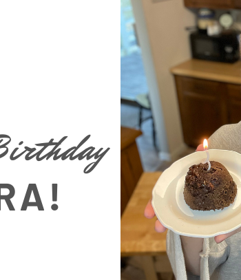 Picture of Sara from Keto on the rise holding a chocolate keto mug cake that is on a white plate with a birthday candle in the cake for the blog keto on the rise